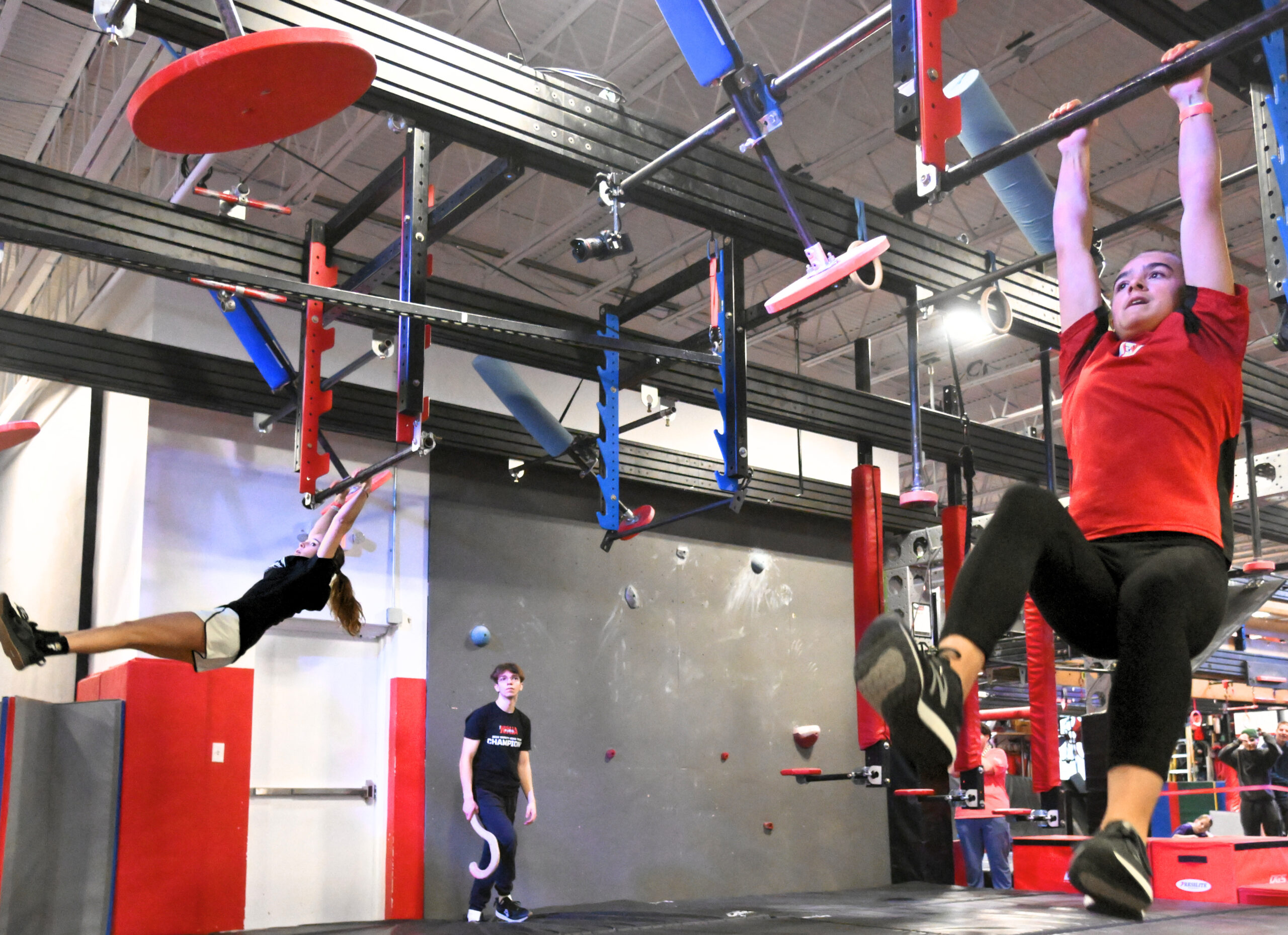 Two teen female ninja athletes compete in a head to head ninja competition. Both athletes are at the same point in the course and racing to get ahead.